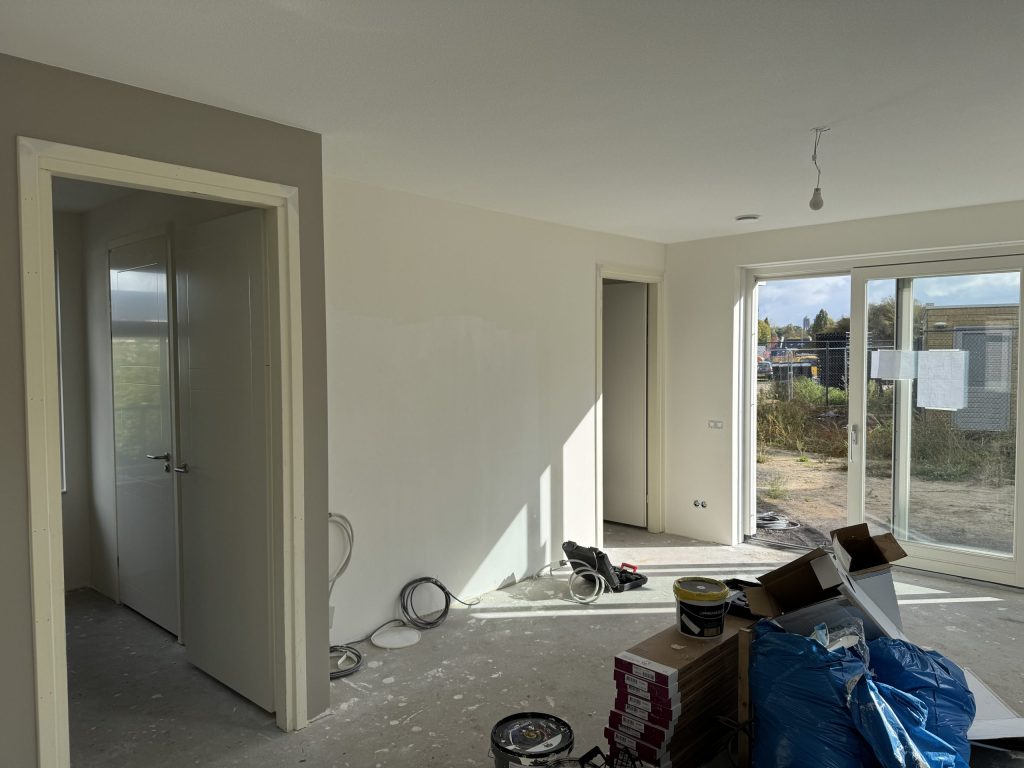 Woonkamer tijdens de afwerking, met verfemmers en dozen op de vloer