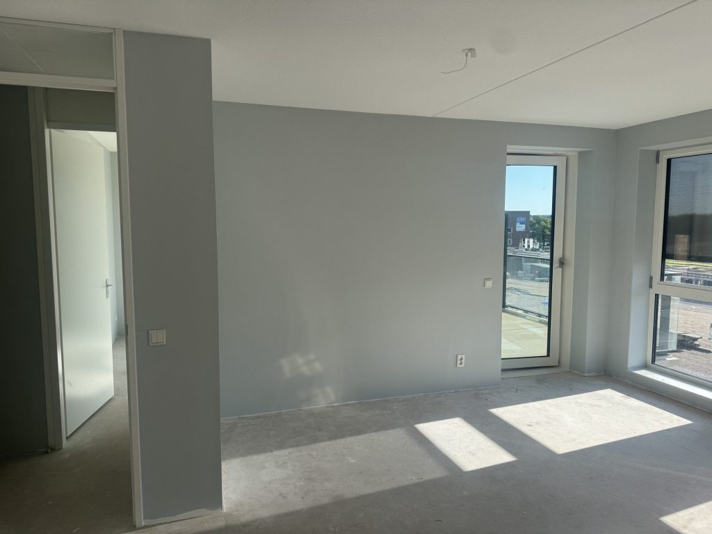 Kamer in een appartement met balkondeur en een lichtgrijze wand