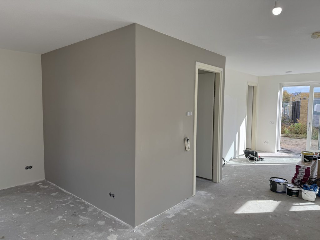 Woonkamer met een net afgewerkte grijze wand en emmers verf op de vloer